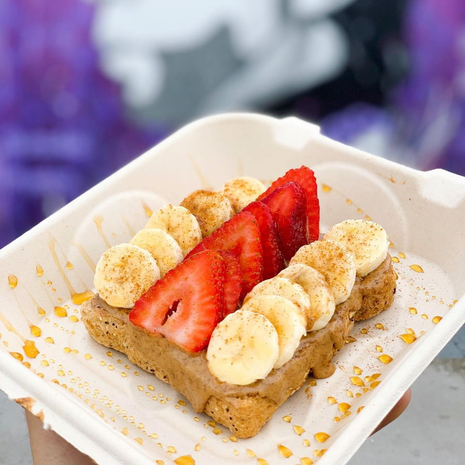 Juice Parlor NoHo's waffle with sliced strawberries, bananas, cinnamon, and honey drizzle in a white container.