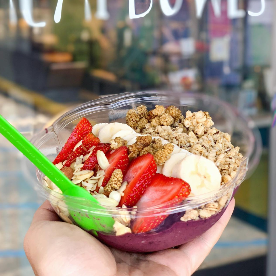 Hand holding a Juice Parlor NoHo acai bowl with strawberries, bananas, granola, and mulberries.
